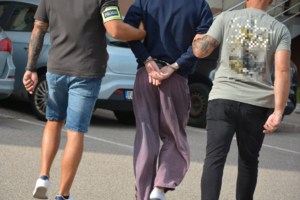 Dwaj funkcjonariusze prowadzą zatrzymanego mężczyznę zakutego w kajdanki.