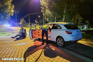 zatrzymany przez policjantów siedzi przy samochodzie.