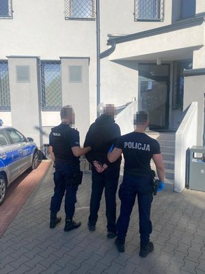 Dwaj policjanci prowadzą zatrzymanego w kajdankach.