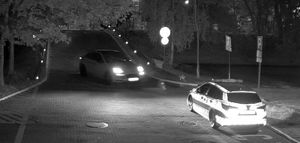 Pora nocna. Jadące auto i zaparkowany radiowóz. Zdjęcie z kamery monitoringu.