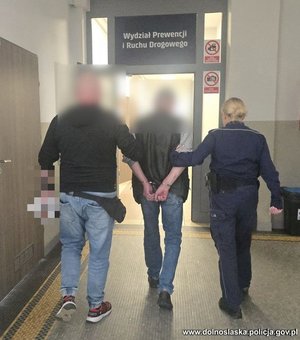 Policjant i policjantka prowadzą zatrzymanego.
