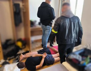 Dwaj mężczyźni zakuci w kajdanki leżą na podłodze. Obok stoją dwaj funkcjonariusze.