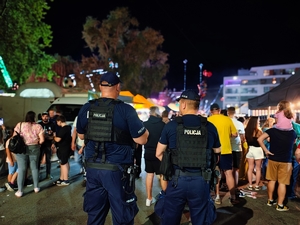 plecy dwóch policjantów. dookoła chodzą ludzie.