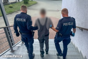 Dwaj umundurowani policjanci prowadzą zatrzymanego.