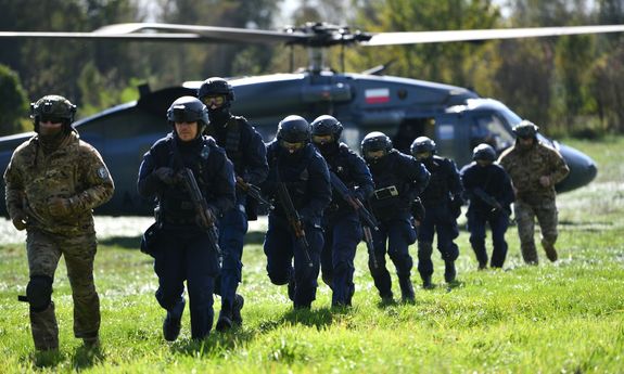 policjanci biegną przed siebie, w tle jest śmigłowiec.