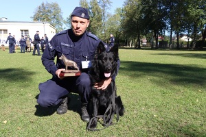 Policjant kuca przy swoim psie. Trzyma statuetkę.