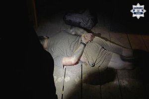 Zatrzymany mężczyzna leży na ziemi - na trzymanych z tyłu rękach ma założone kajdanki.