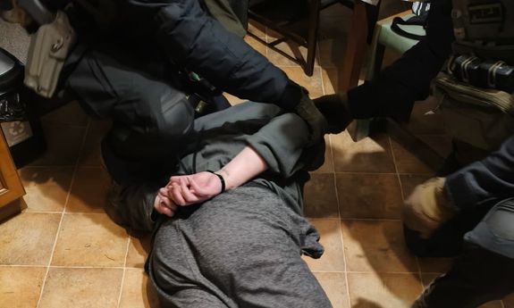 Zatrzymany mężczyzna leży na ziemi w kajdankach na rękach.