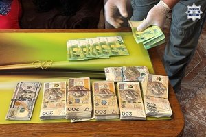Banknoty 200 złotowe leżące w kupkach i banknoty 100 Euro, które rozkłada mężczyzna w rękawiczkach.
