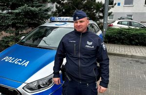 policjant stoi przed radiowozem.