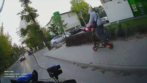 Mężczyzna na hulajnodze jadący chodnikiem.
