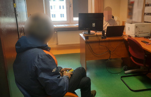 Mężczyzna zatrzymany przez policjantów siedzi na krześle w pomieszczeniu - widok z boku.