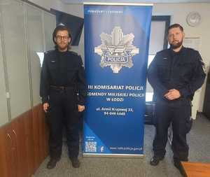 dwóch policjantów stoi obok baneru z logiem jednostki.