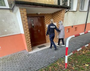 Policjantka prowadzi kobietę do klatki schodowej budynku.