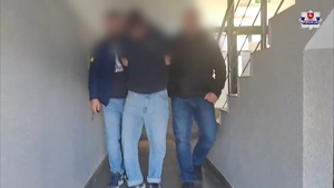 Dwaj policjanci z zatrzymanym mężczyzną w kajdankach.