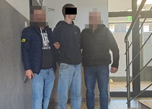 Dwaj policjanci z zatrzymanym mężczyzną w kajdankach.