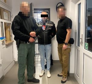 Dwaj policjanci z zatrzymanym mężczyzną zakutym w kajdanki na ręce trzymane z tyłu.