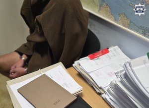 Zatrzymana siedzi przy biurku podczas przesłuchania.