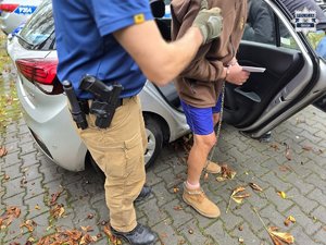 Policjant prowadzi zatrzymaną osobę.