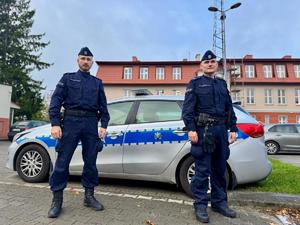 dwóch policjantów stoi przed radiowozem,