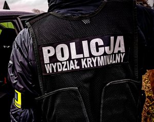Odwrócony tyłem funkcjonariusz z napisem na kamizelce: Policja wydział kryminalny.