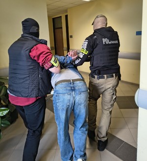 Dwaj policjanci prowadzą zatrzymanego mężczyznę.