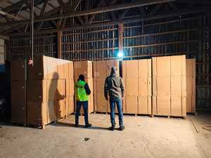 Dwaj policjanci stoją w hali patrzą na kartony wypełnione tytoniem.