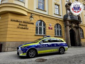 Radiowóz stoi zaparkowany na ulicy przed budynkiem Komendy Powiatowej Policji w Oławie.