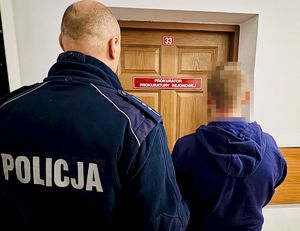 Policjant z zatrzymanym mężczyzną przed  drzwiami z napisem Prokurator Prokuratury Rejonowej.