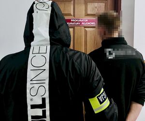 Policjant z zatrzymanym mężczyzną przed  drzwiami z napisem Prokurator Prokuratury Rejonowej.