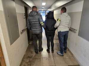 Policjanci stoją z zatrzymaną kobietą.