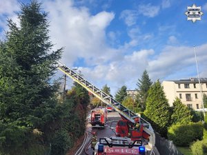 Wóz strażacki i drabina a na wysięgniku strażacy gaszący pożar.