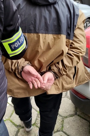 ręka policjanta i plecy zatrzymanego.