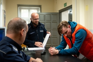 sierż. Tomasz Majowicz na planie serialu Dzielnica strachu z mężczyzną grającym rolę zatrzymanego na posterunku i drugim grającym policjanta.