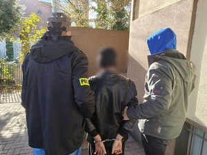 Dwaj policjanci prowadza zatrzymanego mężczyznę.