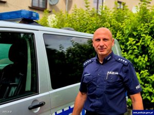 policjant przy radiowozie na tle zielonych krzewów
