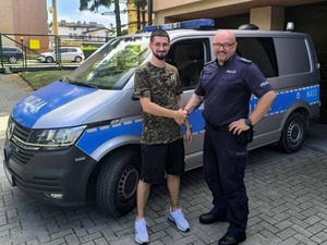 policjant i mężczyzna na tle radiowozu podają sobie rękę w uścisku
