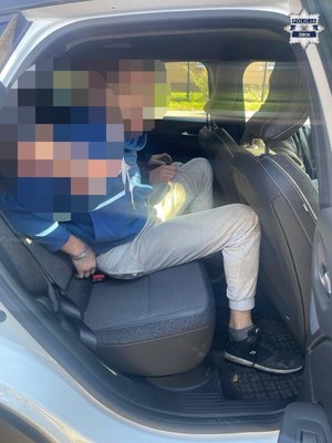 Zatrzymany mężczyzna siedzi w radiowozie na tylnym siedzeniu.