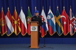 Funkcjonariusz przy mównicy. W tle flagi.