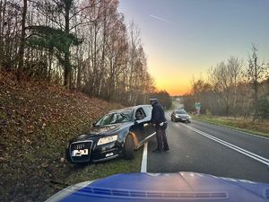 Policjant stoi obok samochodu osobowego stojącego częściowo w rowie.