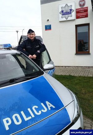 policjant stoi przy radiowozie.