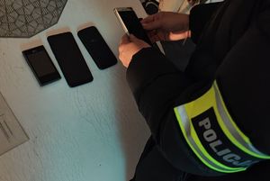 Na stole leżą telefony komórkowe, widać opaskę z napisem Policja.