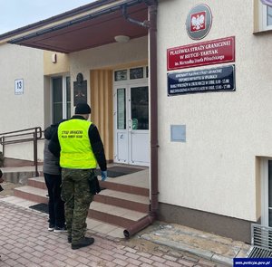 Funkcjonariusz straży granicznej z dwoma nielegalnym imigrantami przed budynkiem straży granicznej.
