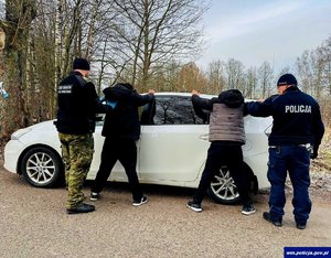 Policjant i funkcjonariusz straży granicznej przy samochodzie z dwoma nielegalnymi imigrantami.