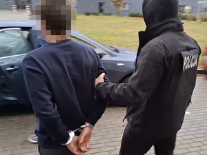 Policjant z zatrzymanym mężczyzną zakutym w kajdanki.