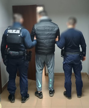 Dwaj policjanci z zatrzymanym przy drzwiach do pokoju.