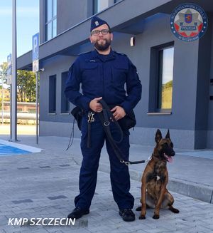Policjant i pies stoją przed budynkiem komendy Policji.