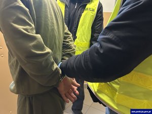Ręce zatrzymanego mężczyzny w kajdankach i  dwaj funkcjonariusze, którzy go prowadzą.