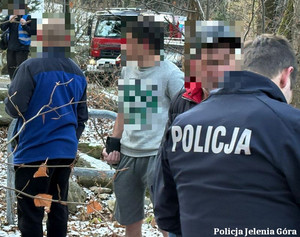 Tłum mężczyzn na dworze i policjant między nimi.