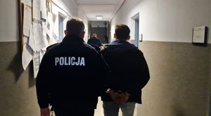 Umundurowany policjant prowadzi zatrzymanego mężczyznę korytarzem.